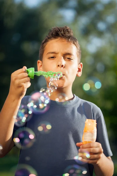 Мальчик раздувает мыльные пузыри в летнем парке — стоковое фото
