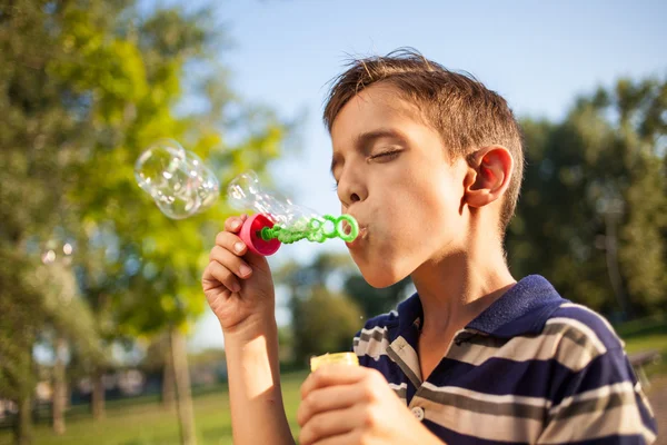 Young  little boy blowing soap bubbles in summer park — Stock Photo, Image