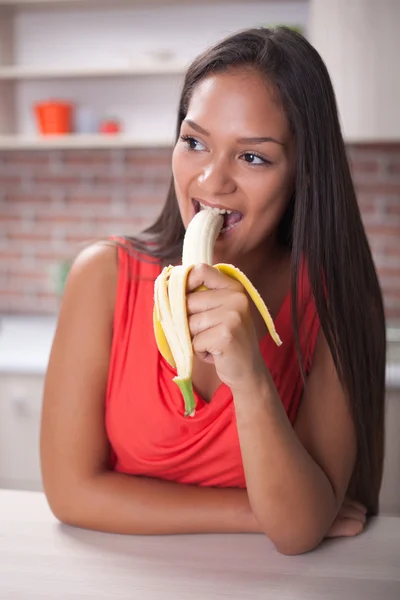 Mujer joven comiendo plátano en la cocina — Foto de Stock