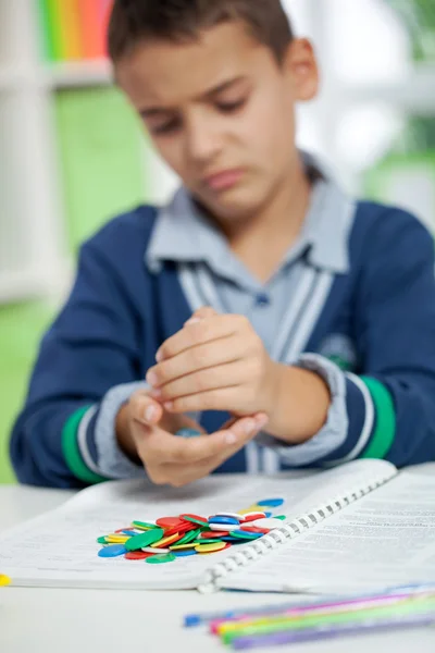 Unhappy schollboy holding chips for calculation — Stock Photo, Image