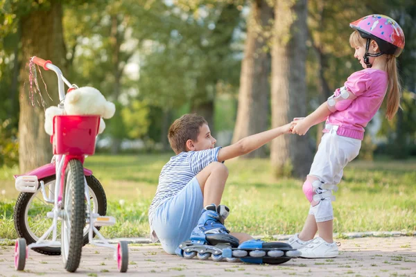 Liten flicka hjälper pojke med rullskridskor stå upp — Stockfoto