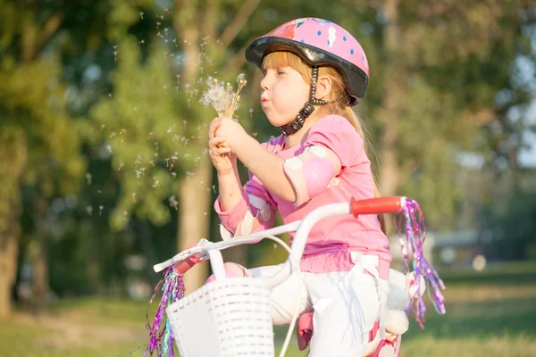 金发碧眼的小女孩，在她吹蒲公英的自行车 — 图库照片
