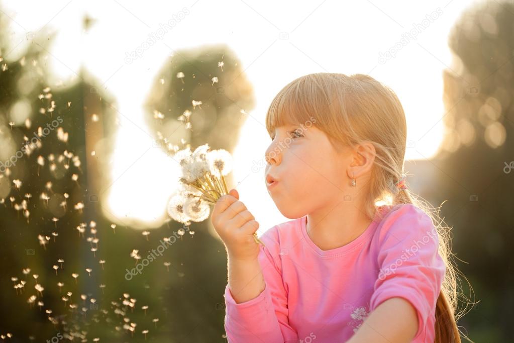 Cute blond little girl blowing a dandelion 