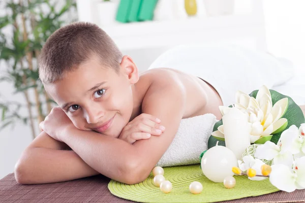 Niño sonriente acostado en la mesa de masaje en el salón de spa —  Fotos de Stock