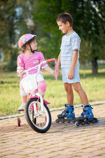 Brother and sister outdoors riding bikes and roller — Stock Photo, Image