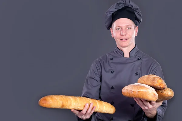 Шеф-кухар Показує хліб у руці на сірому фоні — стокове фото