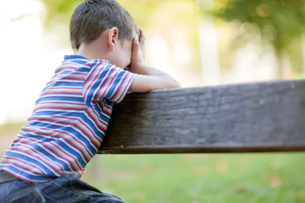 Orphan, unhappy boy sitting on a park bench and crying — Stock Photo, Image