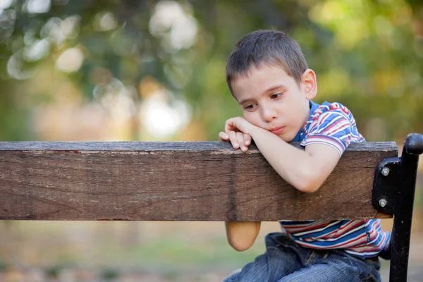 Сирота, несчастный мальчик, сидящий на скамейке в парке и плачущий — стоковое фото
