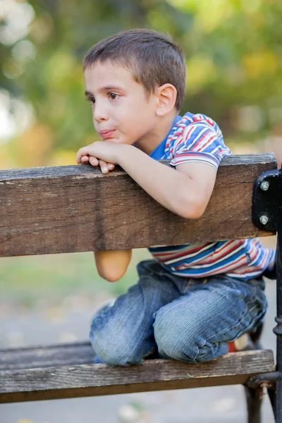 Órfão, menino infeliz sentado em um banco de parque e chorando — Fotografia de Stock