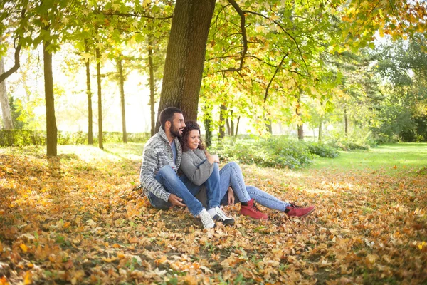 Feliz joven pareja apoyada en un árbol disfrutando del otoño en —  Fotos de Stock