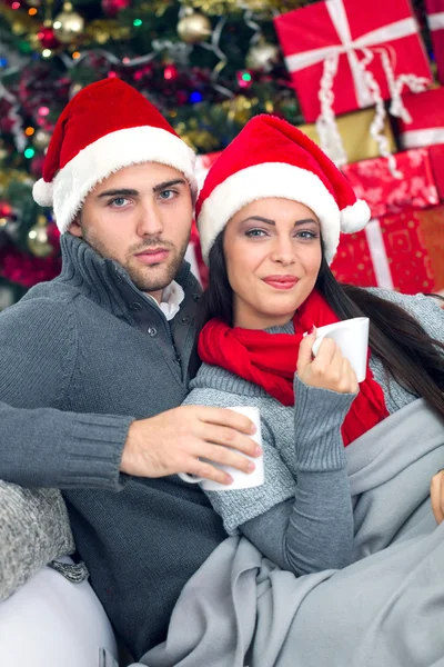 Молодая и улыбающаяся пара в шапке Санты, расслабляющая на Рождество — стоковое фото