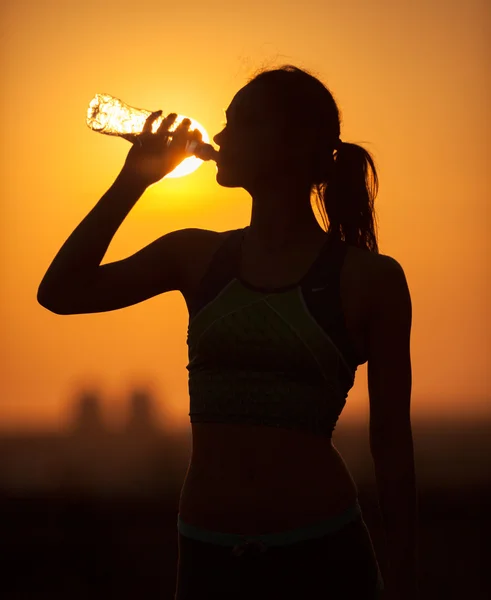 Silhouette of a young sportive woman drinking water — Stock Photo, Image