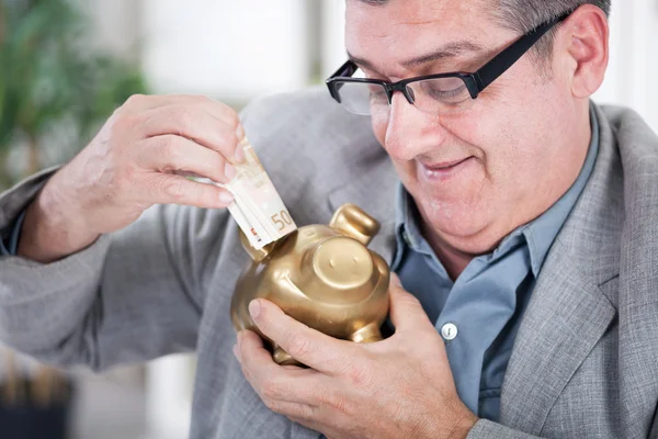 Senior zakenman invoegen van geld naar een piggy bank — Stockfoto