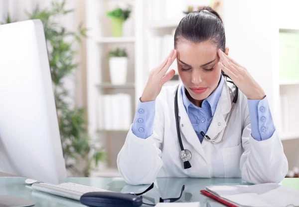 Doctora con los ojos cerrados sentada a la mesa y sosteniendo —  Fotos de Stock