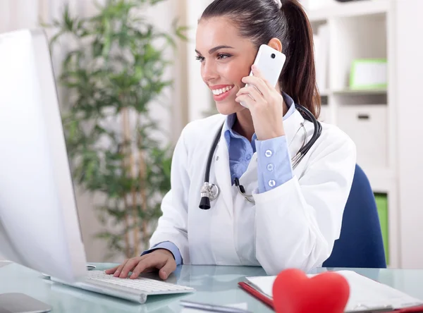 Médica sorridente com telefone e computador workin — Fotografia de Stock