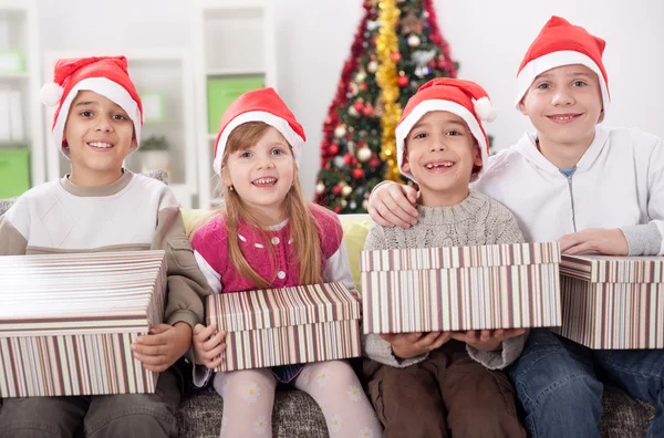 Gruppo di quattro bambini in cappello natalizio con regali — Foto Stock