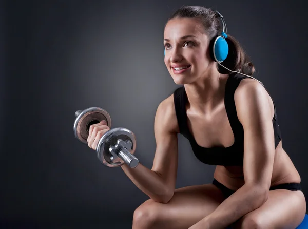 Fitness giovane donna seduta sulla palla sollevare pesi e listeni — Foto Stock