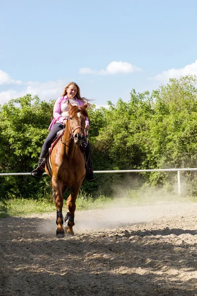 Joven chica sonriente montando su caballo marrón en un campo de entrenamiento — Foto de Stock