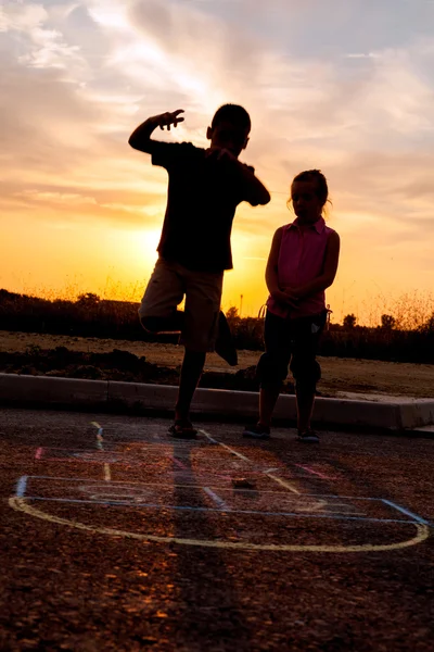 Jonge jongen en een meisje Hinkelspel spelen in de zonsondergang — Stockfoto