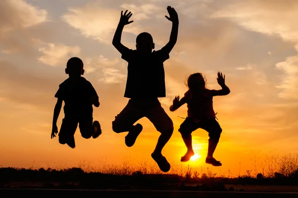 Silhueta pulando de meninos e meninas felizes ao pôr do sol — Fotografia de Stock
