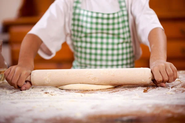 Mains d'un jeune garçon qui tire la pâte dans la cuisine — Photo