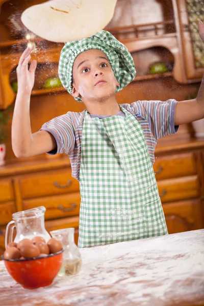Young boy chef, throwing pizza dough into the air — Stock Photo, Image