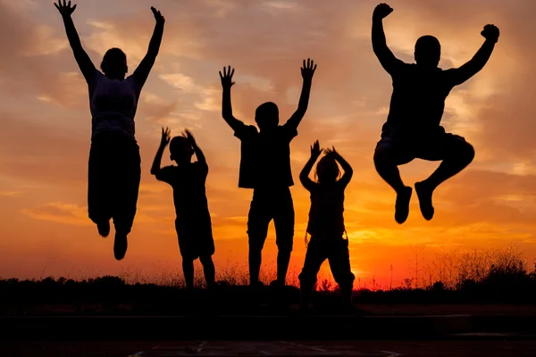 Young happy family jumping silhouettes  at sunset — Stock Photo, Image