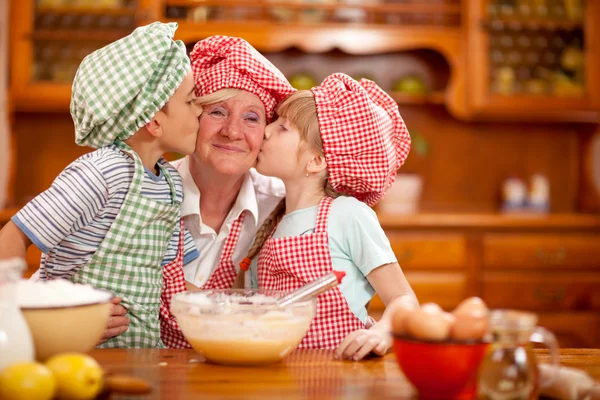 Grandson and granddaughter kiss their grandmother in the kitchen — Stock Photo, Image