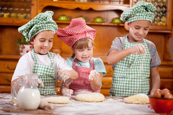 Three funny young child play with a tough in the kitchen — стоковое фото