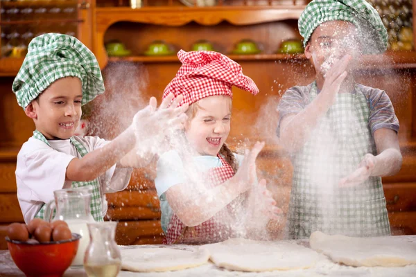 Três engraçado criança apertando as mãos com farinha na cozinha — Fotografia de Stock