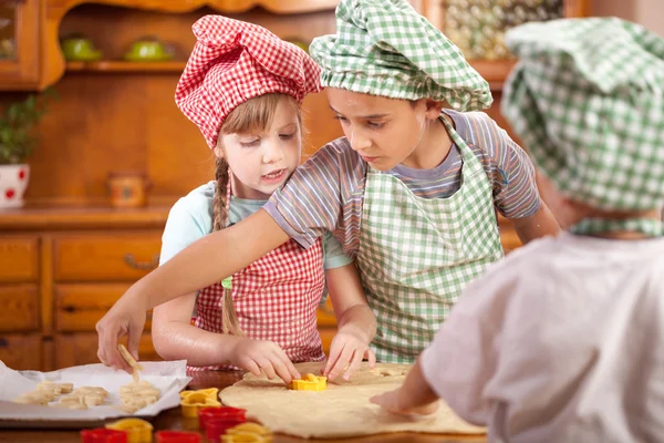 Tři malé dítě připravit soubory cookie v kuchyni — Stock fotografie