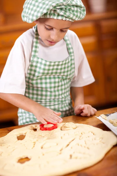 Happy smiling young boy chef in kitchen making tough — стоковое фото