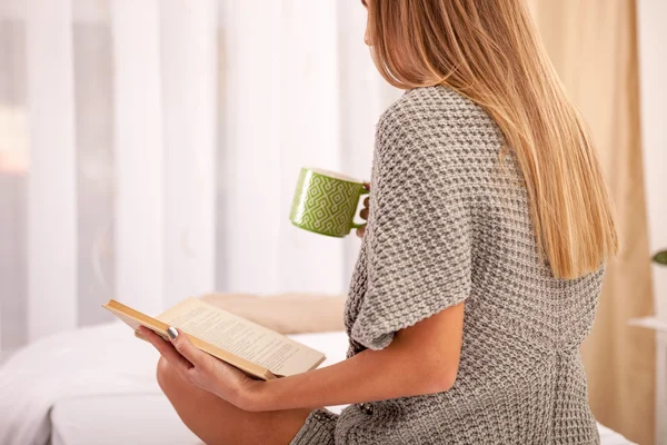 Женщина на кровати со старой книгой и чашкой кофе — стоковое фото