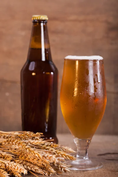 Copo e garrafa de cerveja com orelhas de trigo em madeira — Fotografia de Stock