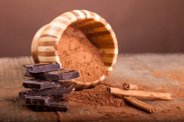 Broken dark chocolate and cinnamon stick on wooden background — Stock Photo, Image