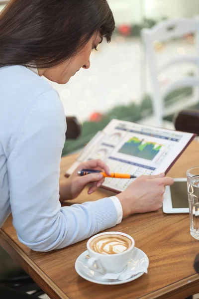 Geschäftsfrau im Coffeeshop blickt in eine grafische Tabelle — Stockfoto
