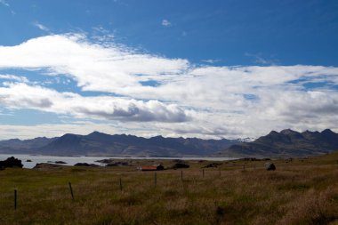İzlanda kıyı şeridinin kırsal manzarası. Dağlar ve Atlantik Okyanusu yakınlarında küçük bir kulübe. Yaz gezisi, Doğu İzlanda.