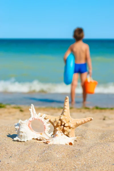 Ребенок с игрушками, смотрящий на море — стоковое фото