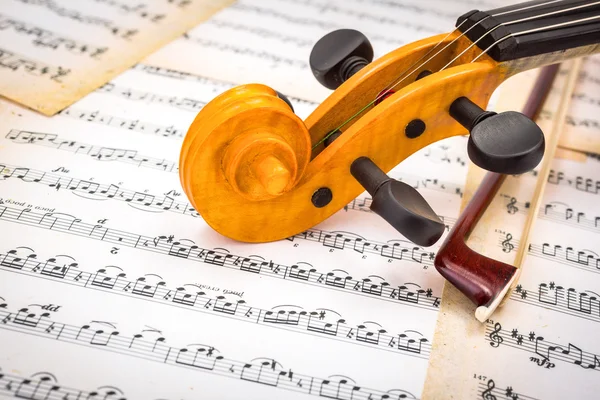 Close view of violin scroll and bow on score — Stock Photo, Image