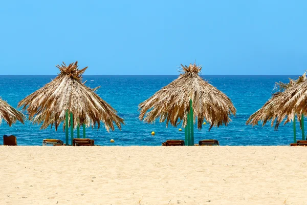 Blauwe zee, gouden zand en ligbedden op het strand — Stockfoto