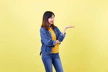 Çekici, sevimli, sevimli, Asyalı, esmer, ceketli, kot pantolonlu, gülümseyen, sarı arka plan güzelliği ve yüz ifadelerinden izole edilmiş kameraya bakan bir kadın.