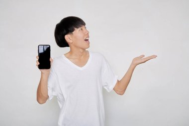 Asyalı yakışıklı, beyaz bir tişört giyen, beyaz bir akıllı telefon ekranı gösteren ve avuç içini gösteren bir portre.