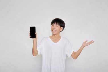 Asyalı yakışıklı, beyaz bir tişört giyen, beyaz bir akıllı telefon ekranı gösteren ve avuç içini gösteren bir portre.