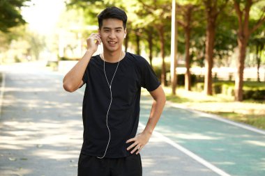 Genç yakışıklı Asyalı adam dışarıda egzersiz yapıyor. Parkta müzik dinliyor..
