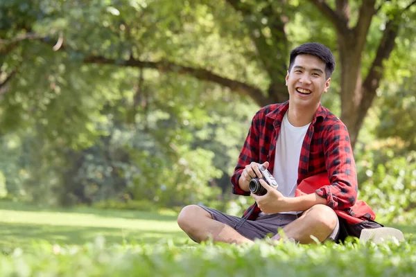 夏の日に芝生のフィールドに座っている若いアジアの男のバックパッカーハンサムな男は休日の休暇にアウトドアライフスタイルで楽しむ — ストック写真