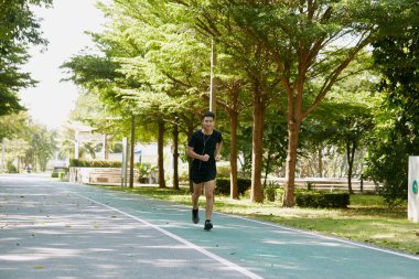 Yakışıklı Asyalı genç bir sporcunun portresi. Koşu yapıyor. Akıllı telefon konseptiyle müzik dinliyor.