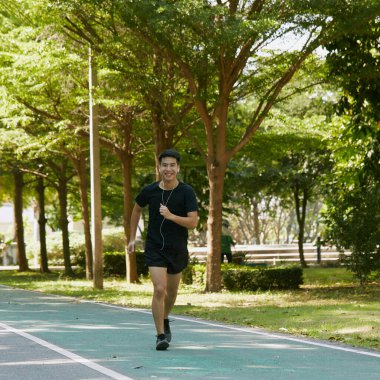 Yakışıklı Asyalı genç bir sporcunun portresi. Koşu yapıyor. Akıllı telefon konseptiyle müzik dinliyor.