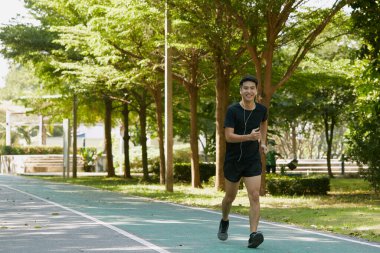 Yakışıklı Asyalı genç bir sporcunun portresi. Koşu yapıyor. Akıllı telefon konseptiyle müzik dinliyor.