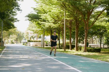 Yakışıklı Asyalı genç bir sporcunun portresi. Koşu yapıyor. Akıllı telefon konseptiyle müzik dinliyor.