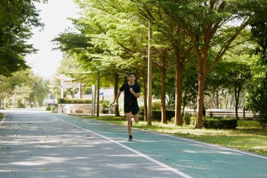 Yakışıklı Asyalı genç bir sporcunun portresi. Koşu yapıyor. Akıllı telefon konseptiyle müzik dinliyor.